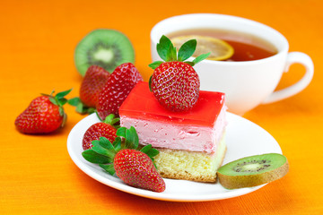 lemon tea, kiwi,cake and strawberries lying on the orange fabric