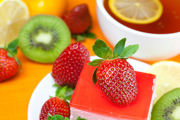 Fototapeta na wymiar lemon tea, kiwi,cake and strawberries lying on the orange fabric