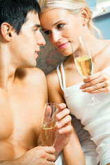 Young happy amorous couple with champagne at bedroom