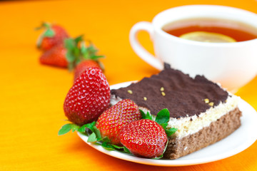 lemon tea, cake and strawberries lying on the orange fabric