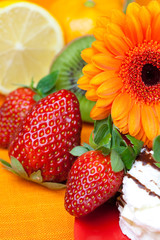 lemon ,gerbera,cake and strawberries lying on the orange fabric