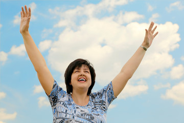 Fototapeta na wymiar brunette plumpy mature woman smiling, hands up, blue sky