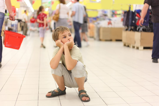 Little Boy Sitting Alone On Hunkers In Big Store