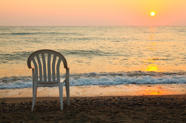 white plastic chair is on seashore. beautiful orange sunset