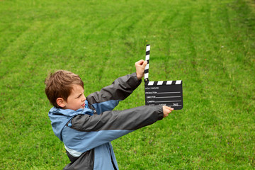 boy with cinema clapper board in hands standing on field