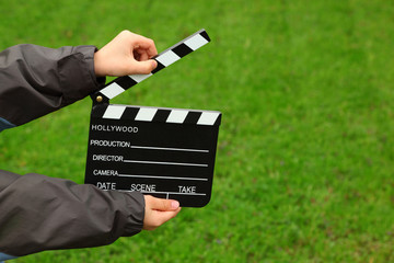 Cinema clapper board in hands of boy on field with grass