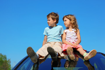little boy and girl sitting on car roof on blue sky