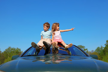Fototapeta na wymiar little boy and girl sitting on car roof on blue sky