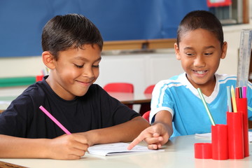 Two schoolboys helping each other learn in class during lessons