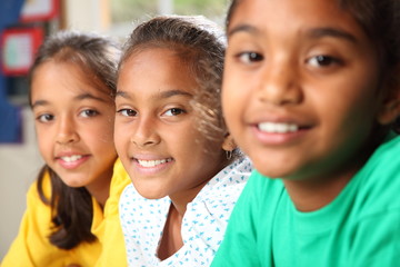 Row of three smiling young school girls sitting in class