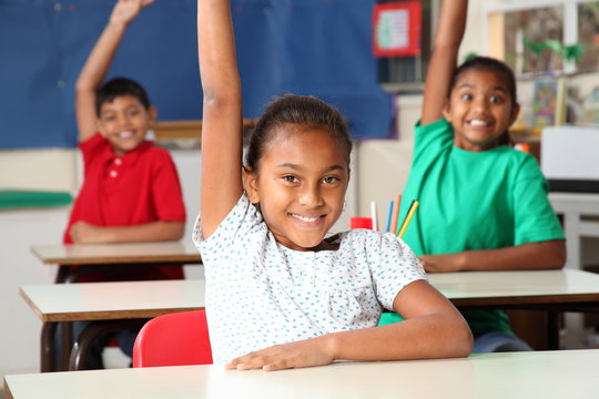 Three young school children arms raised in class