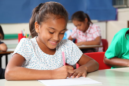 Young schoolgirl in classroom busy writing at desk
