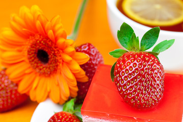 gerbera, lemon tea, cake and strawberries lying on the orange fa