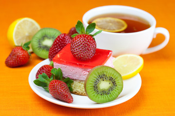 lemon tea, kiwi,cake and strawberries lying on the orange fabric