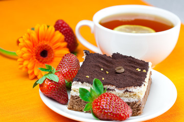 gerbera, lemon tea, cake and strawberries lying on the orange fa
