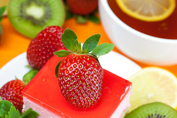 lemon tea, kiwi,cake and strawberries lying on the orange fabric