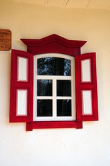 Red shuttered window on white wall