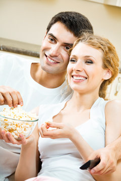 Young happy smiling couple eating popcorn and watching TV