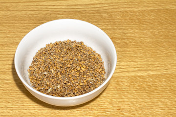 Bowl of wheat grain in white bowl on wooden table