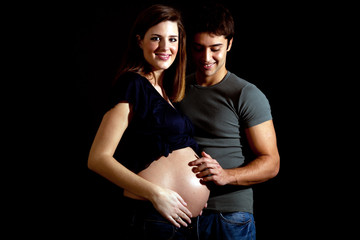Mom and dad embracing pregnant belly isolated on black