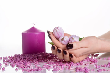 Candle and cupped hands with dark manicure holding tulips