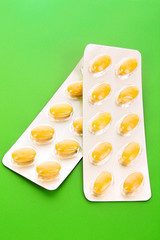 Yellow capsules of vitamins on a green background