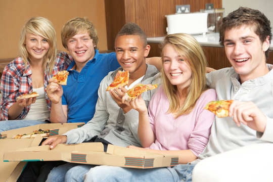 Group Of Teenage Friends Sitting On Sofa At Home Eating Pizza