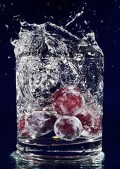 Bunch of red grapes falling down in glass with water on deep blu