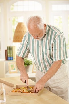 Elderly man slicing up pizza.
