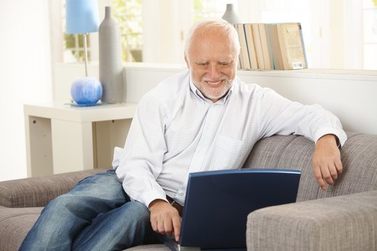 Older man smiling at computer screen at home