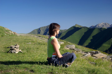 Naklejka na ściany i meble Kobieta siedzi na trawie w górach relaksujących