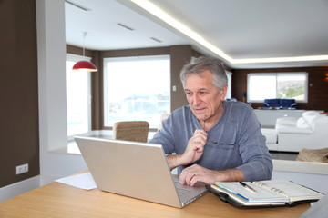 Fototapeta na wymiar Senior man at home in front of laptop computer