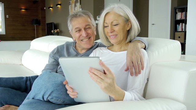Senior couple in sofa using electronic tab