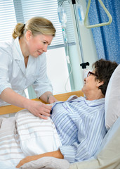 Nurse cares for a female patient lying in bed in hospital