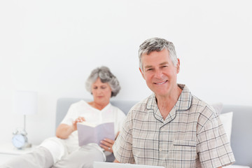 Man working on his laptop while his wife is reading