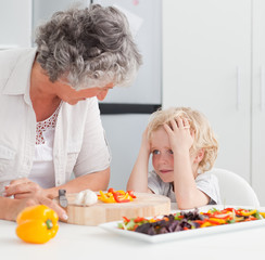 Little boy looking at his grandmother cooking at home