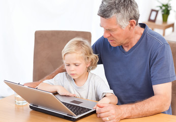 Lovely boy and his grandfather looking at their laptop