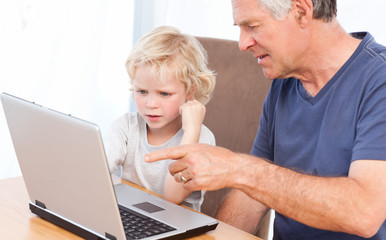 Lovely boy and his grandfather looking at their laptop