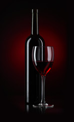 Bottle and glass of red wine on black background