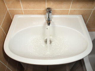 White modern ceramic handbasin and chrome tap, water running.
