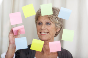 seniorin klebt postits auf eine glasscheibe