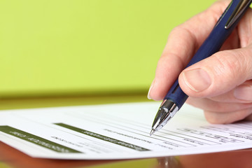 Hand with Pen Signing Form Closeup on Green Background