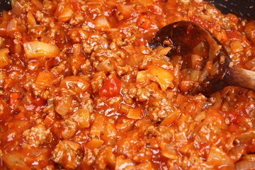 Bolognese sauce being fried on a pan with a wooden ladle