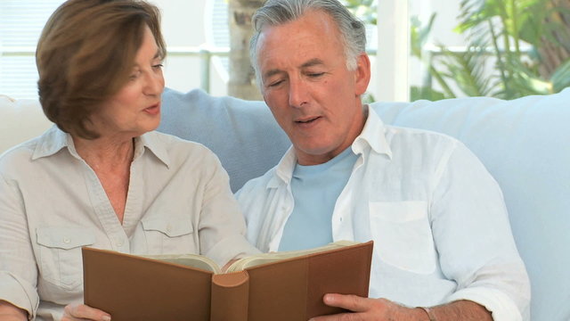 Aged couple looking at a photos album in the living room