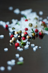 Seasalt, thyme and colorful peppercorns on a shiny black.