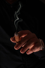 The man's hand with hours, holds a smoking cigar