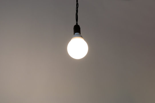 Round  energy saving  lamp on a black wire on light background
