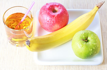Banana, green and red apples on plate and glass of juice