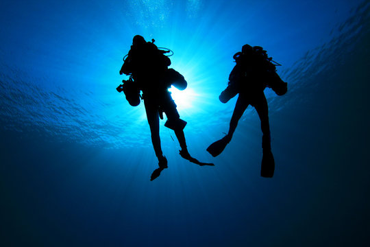 Two Technical Divers silhouetted against sun
