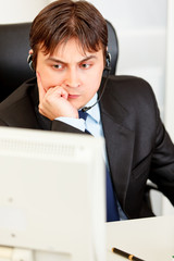 Serious businessman with headset  looking at computer monitor.